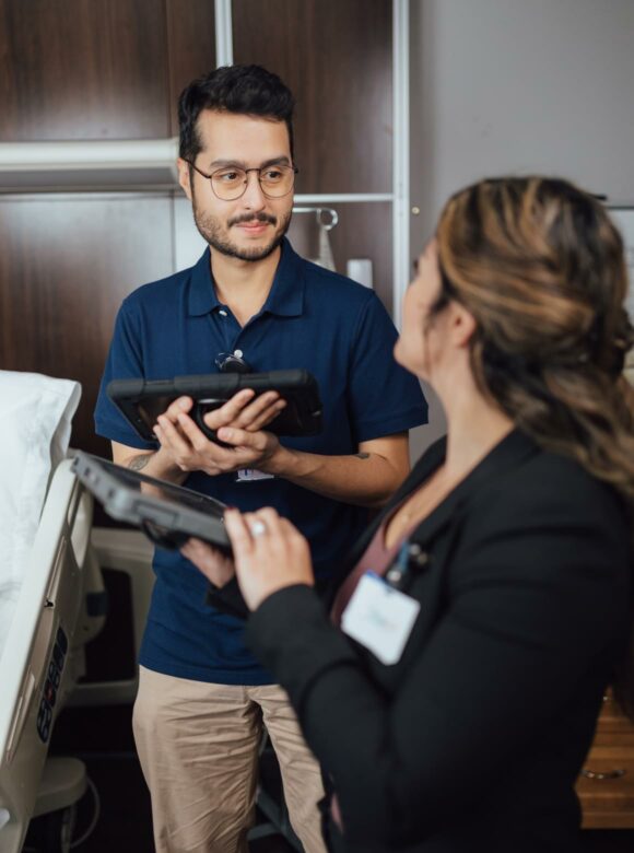 Male healthcare employee assisting female colleague with tablet computer in office setting