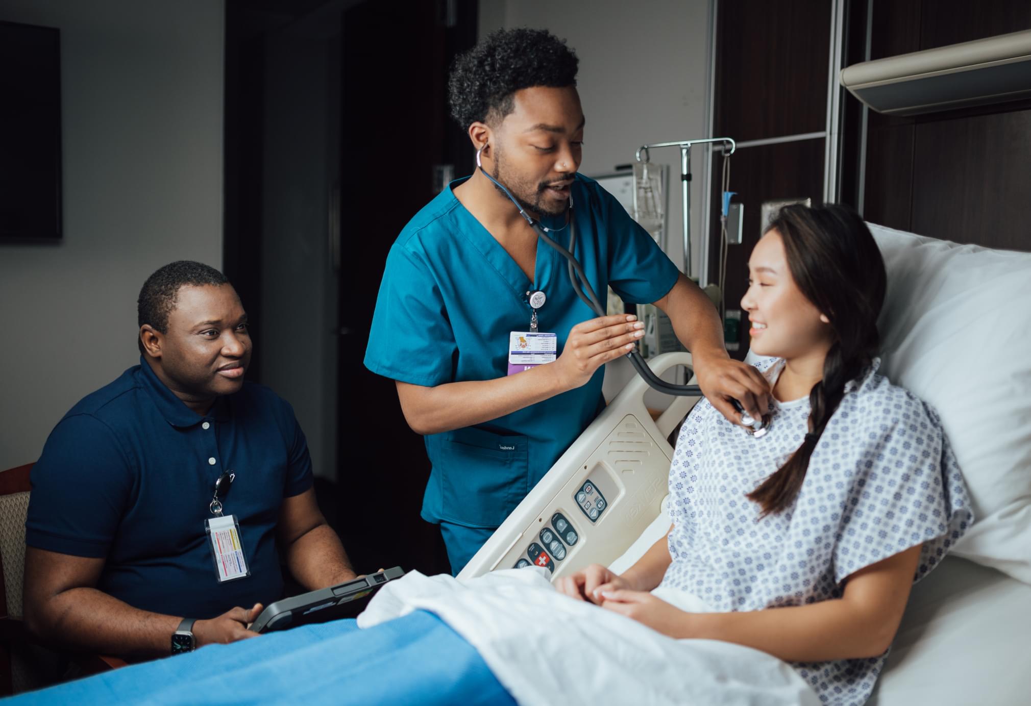 Healthcare workers consulting with patient in hospital room, using medical technology devices