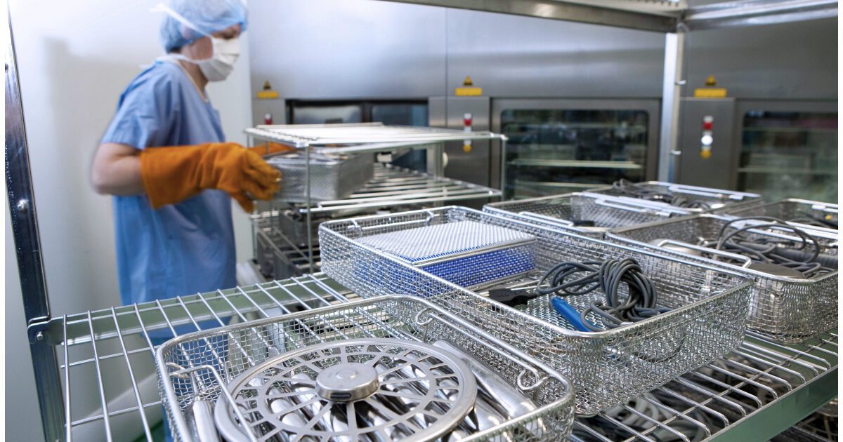 Sterile processing technician puts surgical instruments into automated washer in hospital lab