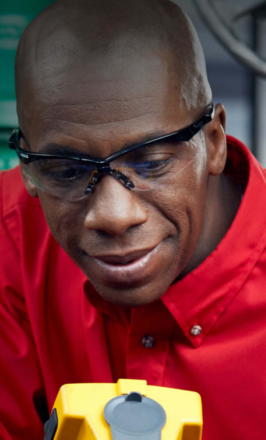 Close-up portrait of a focused male industrial worker wearing red shirt and safety glasses