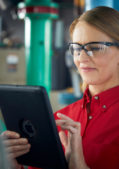 Technician in red shirt and safety glasses using tablet computer in industrial workplace setting