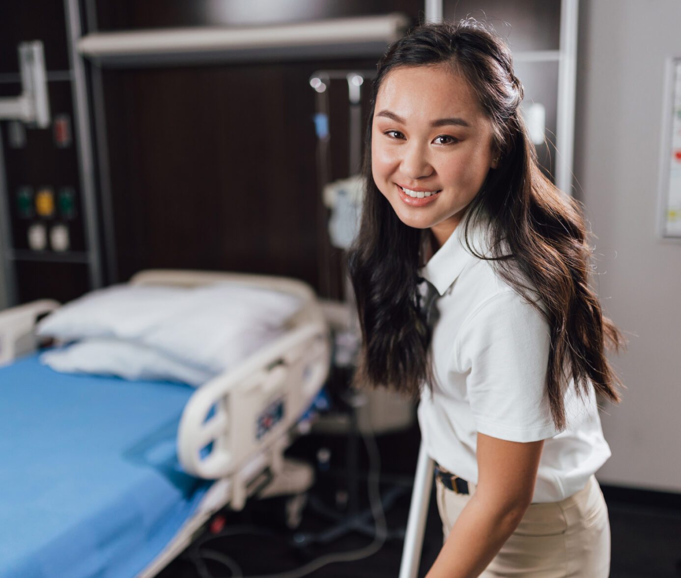 Smiling healthcare worker in hospital room with patient bed in background