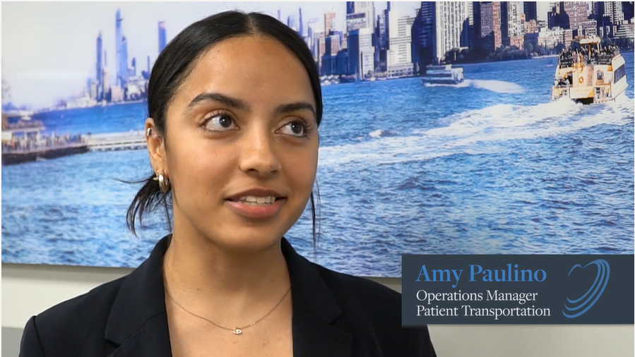 Young woman with dark hair smiling in front of New York City skyline with boats in river